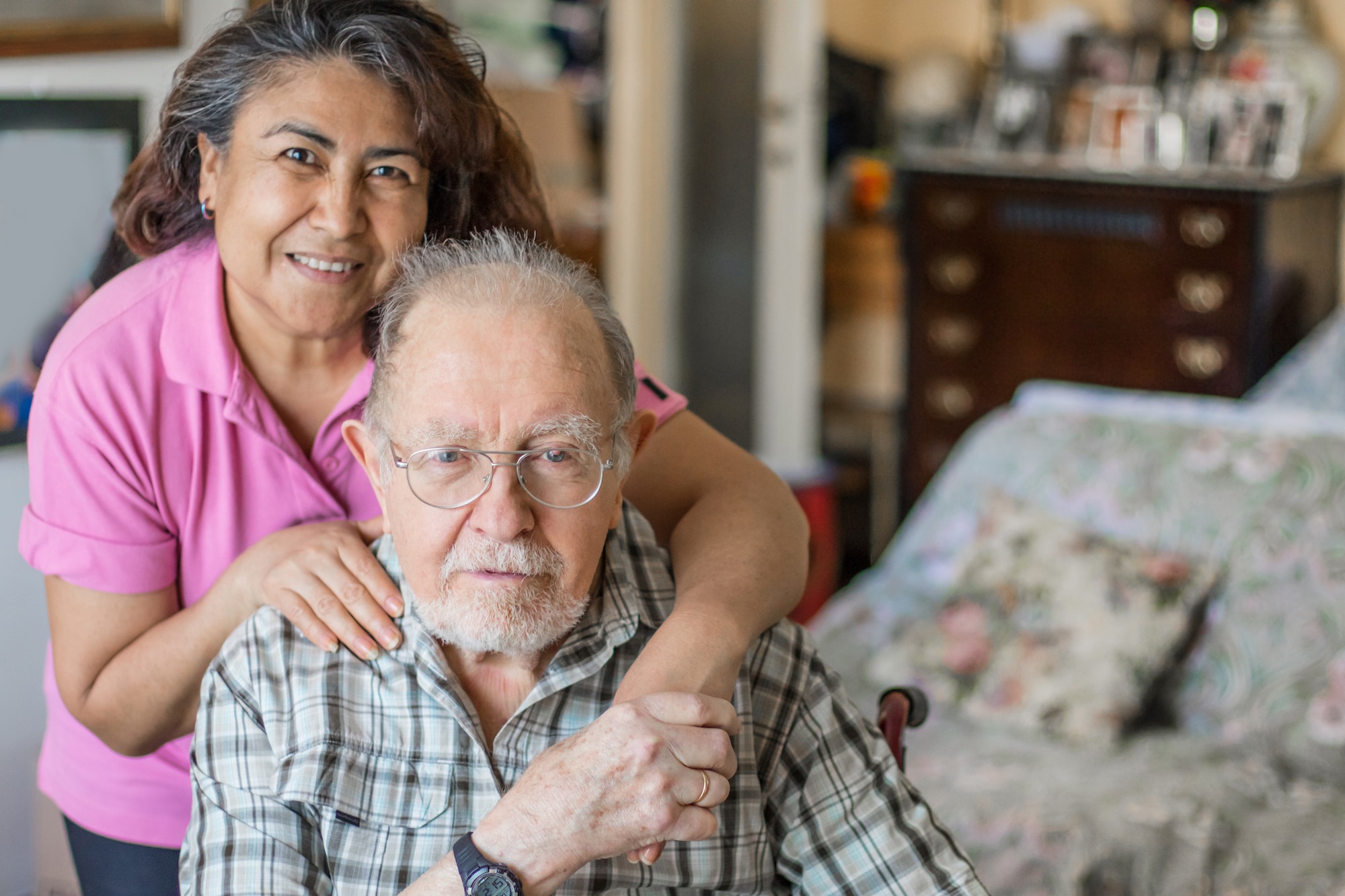 A woman is hugging an older man in his home.